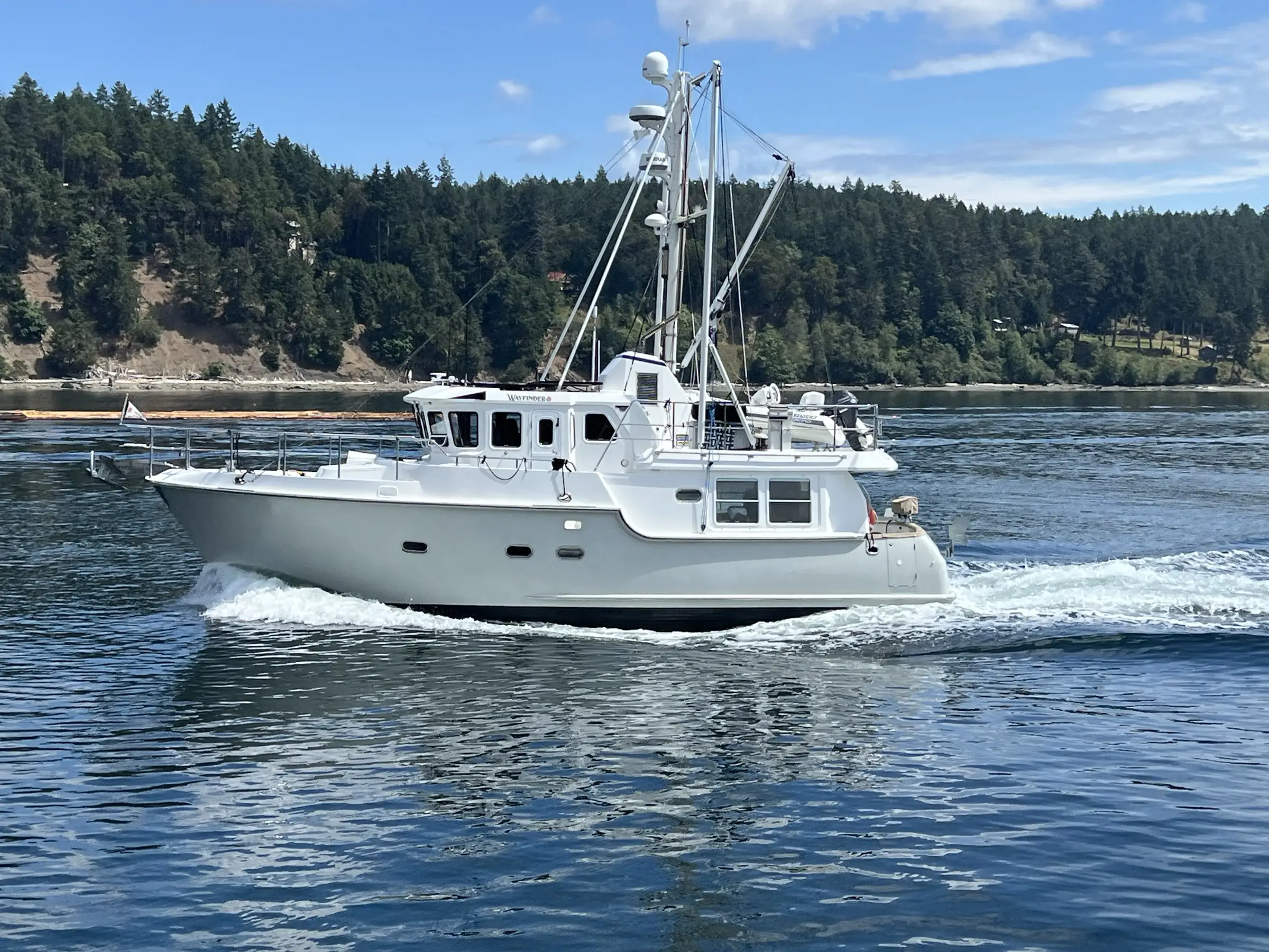 A Pacific Northwest yacht underway along a forested shoreline